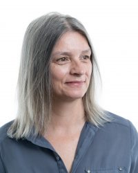 Headshot of a woman in a light blue shirt smiling away from the camera